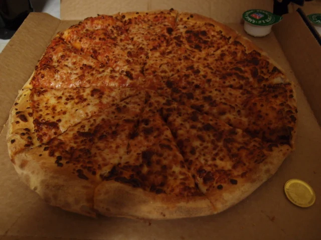A Marguerita pizza in its delivery box, a pot of garlic and herb dip at the top and a gold Casascius bitcoin resting on the cardboard